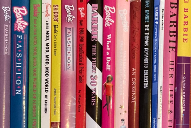 Image direction: collector reference material in use - books, catalogues or comparison sheets beside a doll and accessories. The visual should communicate study rather than shopping.