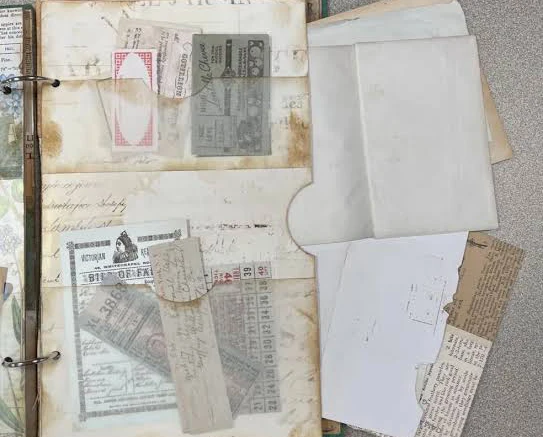 Image direction: archival storage of mixed ephemera - appropriately sized boxes, folders and sleeves with different paper and photographic materials visible. Avoid a generic museum archive shot with no material detail.
