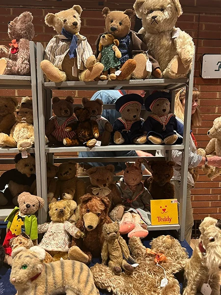 Image direction: a specialist fair, collector table or close handling scene where antique bears, artist bears, makers and repair expertise visibly coexist. The image should communicate comparative learning rather than simple shopping.